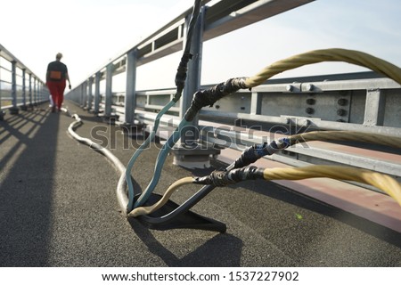 Power electric cable on the bridge. Power cable on the pedestrian area of the road. A man walking by an electric cable.