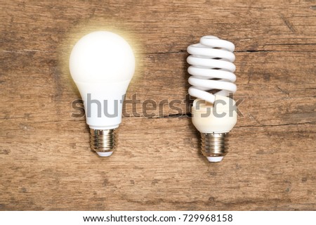 Power energy saving concept.Spiral compact-fluorescent (CFL) bulbs vs new  Light Emitting Diode ( LED ) light bulb with light on on wooden background.