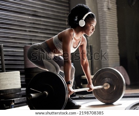 Power, fitness and headphones of a woman with barbell weight lift exercise, workout or training in wellness gym. Sports black woman listening to motivation music for muscle, strength and health