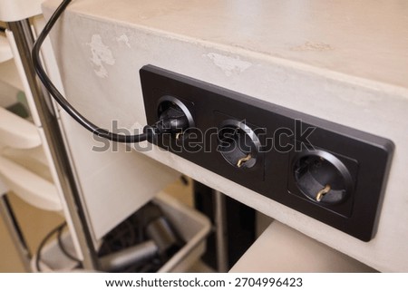Power hub setup, Closeup of mounted power strip with multiple connections and cables, IT technician arranging cords and connecting devices on cluttered tech workstation