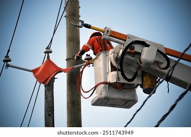 Power lineman performing maintenance on electrical lines from an elevated work platform. Ensuring safe and reliable electrical service. High visibility vest and hat blue sky fixing cables. - Powered by Shutterstock