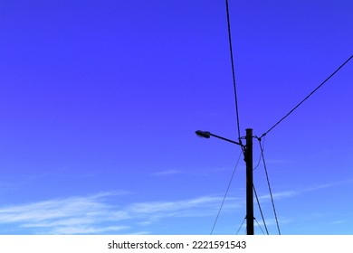 Power Lines In The Air. One Wooden Pole With A Lamp. Blue Sky In The Background. Copy Space For Extra Text. Sweden, 2022.