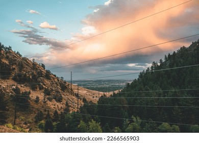 Power Lines running through mountainous valley with clouds overhead during golden hour