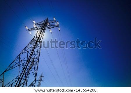 a power mast of a high voltage transmission line against blue sky with sun