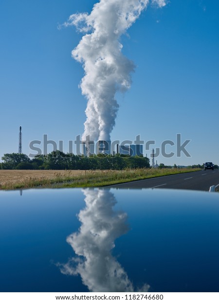 Power Plants:\
The water vapor clouds from two cooling towers of a lignite-fired\
power station are reflected in the early morning sun on the roof of\
a car parked on the\
roadside