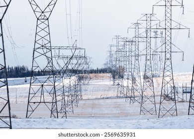 Power pole rows with electrical lines supplying energy to the power grid overlooking winter prairie fields in Rocky View County Alberta Canada.