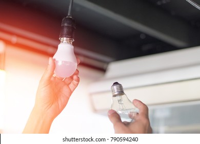 Power saving concept. Asia man changing compact-fluorescent (CFL) bulbs with new LED light bulb.
