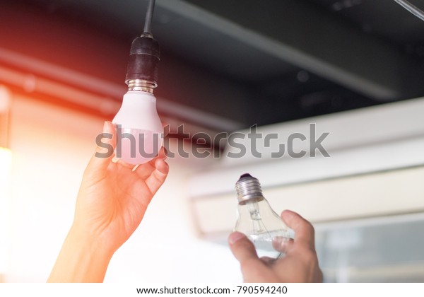 Power saving concept. Asia man\
changing compact-fluorescent (CFL) bulbs with new LED light\
bulb.\

