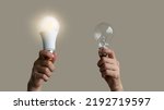 Power saving concept. Hands holding new Light Emitting Diode ( LED ) light bulb with light on and blur spiral compact-fluorescent (CFL) bulbs behind for copyspace.