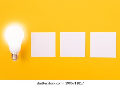 A Power Saving Lamp with White Note Paper Lying on Yellow Table, Blank Template with Copy Space - Top View, Flat Lay