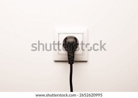 Power socket with inserted plug on white wall, space for text. Electrical supply