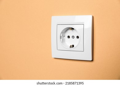 Power socket on pale orange wall, space for text. Electrical supply