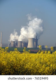  Power station with smoking cooling towers behind a canola field