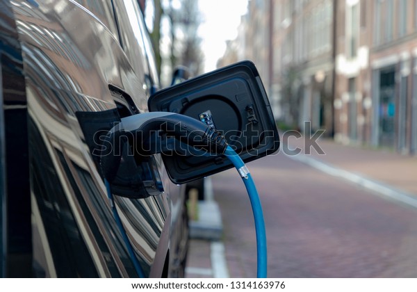 Power supply connect to electric\
vehicle for charging battery, Charging an electric car in public\
station by the street, Green energy, Amsterdam,\
Netherlands.