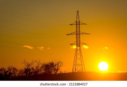 Power transmission towers or electricity pylons with golden sky and clouds. Silhouetted electric pylon with power line at sunset.