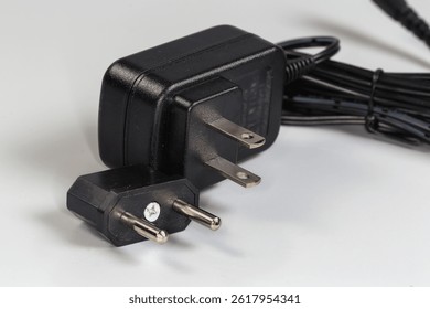 Power unit for various gadgets with American AC two-pronged plug and separately adapter to Euro plug on a gray background, close-up in selective focus