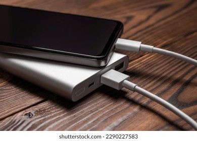 Powerbank and charge smartphone on wooden table. - Shutterstock ID 2290227583