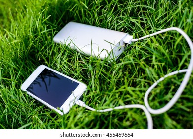 Powerbank Charging White Smartphone On Grass