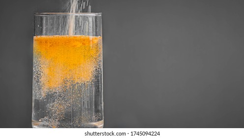 Powered Orange Drink Mix Being Poured Into A Clear Glass Of Water