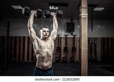 Powerful athletic man training shoulder muscles with heavy dumbbells doing overhead in gym. Healthy lifestyle concept