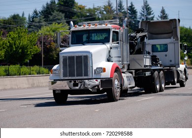 A Powerful Big Rig Semi Truck Tractor Tows A Broken Semi Truck On A Highway With Green Trees To The Repair And Diagnostic Site In A Specialized Repair Shop With A Qualified Mechanics