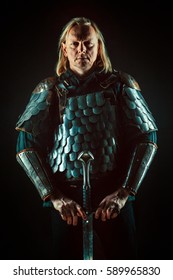 Powerful blond knight with the sword on the dark background