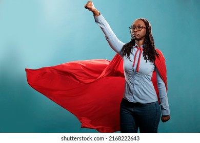 Powerful and brave young superhero woman wearing hero costume while posing as flying on blue background. Proud and strong african american justice defender looking ambitious while looking at camera. - Powered by Shutterstock