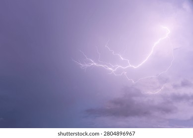 A powerful bright lightning bolt branches across a deep purple overcast sky during a intense thunderstorm, showcasing the raw energy and dramatic beauty of severe weather events.