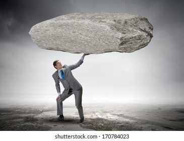 Powerful businessman holding huge stone above head - Shutterstock ID 170784023