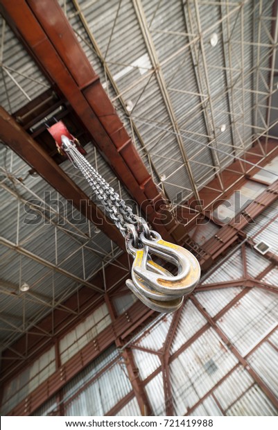 Powerful cargo hooks hang on a\
long load chain. Hook suspension of a bridge crane. Industrial\
shop.