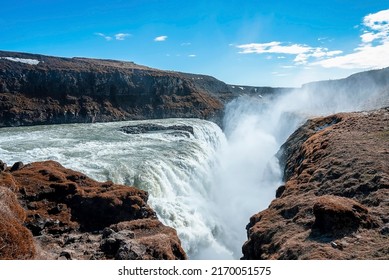 Powerful Cascades Of Gullfoss Waterfall In Golden Circle. Beautiful Fog Of Falling Water Amidst Rock Formation Against Blue Sky. Idyllic Natural Scenery In Valley.