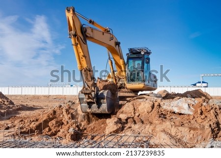 A powerful caterpillar excavator digs the ground against the blue sky. Earthworks with heavy equipment at the construction site