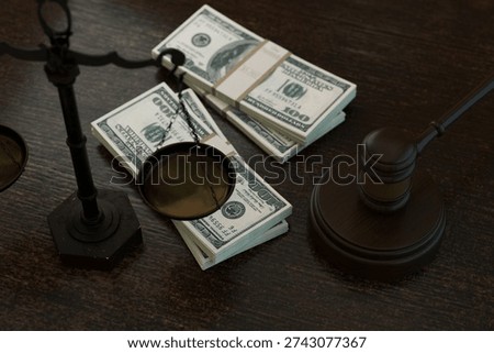 powerful conceptual shot featuring stacks of US hundred dollar bills balanced on legal scales next to a wooden judges gavel. Represents legal costs, corruption, bribery, and financial justice. Law