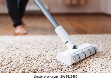 Powerful cordless vacuum cleaner with white cyclonic dust collection technology in hand, cleans the carpet in the house near the sofa. Close-up