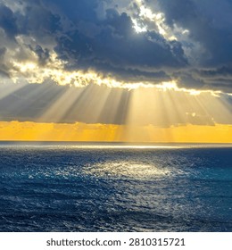 Powerful crepuscular rays stream through dark, moody clouds, illuminating the ocean surface with a golden glow.