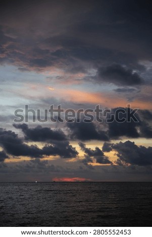 Powerful Dark Clouds Hanging Over the Ocean Horizon with Colorful Sunset Twilight Sky
