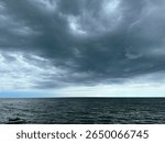 Powerful and dramatic dark clouds rolling over a calm sea, captured just before a storm. The ocean horizon meets a swirling sky, creating a dramatic and emotional scene.