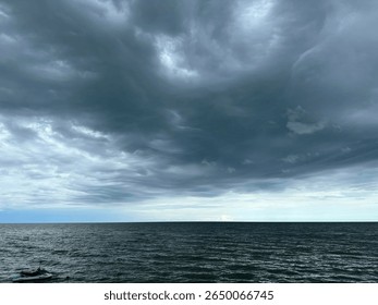 Powerful and dramatic dark clouds rolling over a calm sea, captured just before a storm. The ocean horizon meets a swirling sky, creating a dramatic and emotional scene.