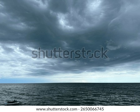 Powerful and dramatic dark clouds rolling over a calm sea, captured just before a storm. The ocean horizon meets a swirling sky, creating a dramatic and emotional scene.