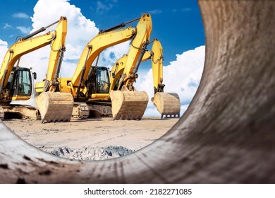 Powerful excavators at a construction site viewed from a large diameter pipe. earth moving construction equipment. Lots of excavators. Laying of underground communications