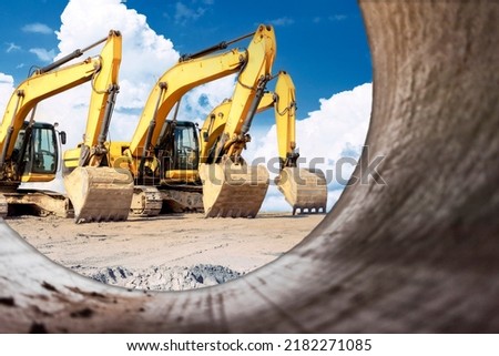 Powerful excavators at a construction site viewed from a large diameter pipe. earth moving construction equipment. Lots of excavators. Laying of underground communications