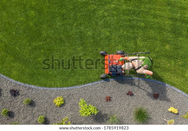 Powerful Gasoline Lawn\
Aerator Job For Controlling Lawn Thatch, And Reducing Soil\
Compaction. Backyard Grass Field Maintenance. Caucasian Gardener in\
His 40s. Aerial View.
