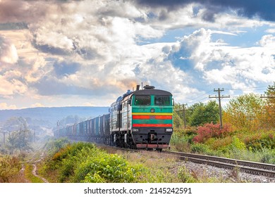 A Powerful Green Diesel Locomotive Pulls A Long Train Loaded With Cement And Building Materials. Freight Railway Transportation. Sunny Weather.