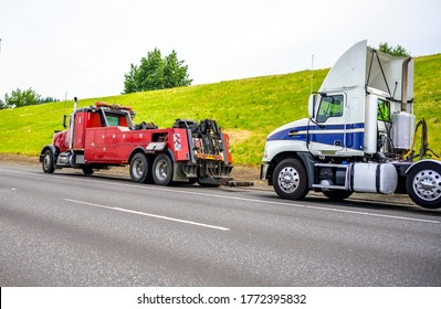 Powerful heavy-duty big rig mobile tow semi truck with emergency lights and towing equipment prepare to tow broken white big rig semi tractor standing out of service on the road side