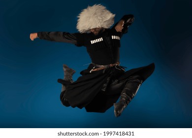 Powerful jump of Georgian dancer man in traditional costume isolated on blue.. High quality picture of authentic Caucasian dancers performing on dark blue matte background