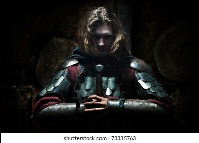 Powerful Knight In The Armor With The Sword. Dark Background.