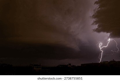 Powerful lightning bolt illuminates a dramatic thunderstorm sky above an urban skyline. Dark storm clouds and moody atmosphere, ideal for weather, climate, energy, danger, and dramatic background concepts.