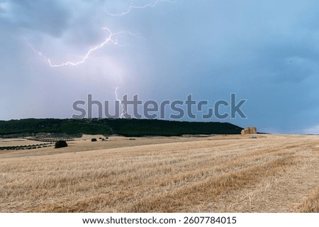 A powerful lightning bolt illuminates a vast dry field as dark storm clouds gather above the horizon.
