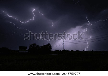 Powerful lightning bolts illuminating the night sky over a rural landscape, creating a dramatic and awe inspiring scene