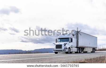 Powerful long haul big rig industrial grade diesel semi truck transporting commercial food cargo in refrigerated semi trailer running on the flat road with sky and hills view in Columbia Gorge
